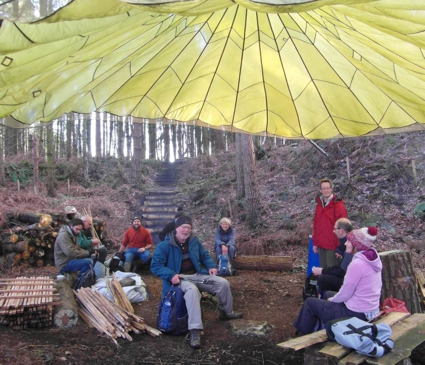 A group of volunteers having lunch under a parachute tarp